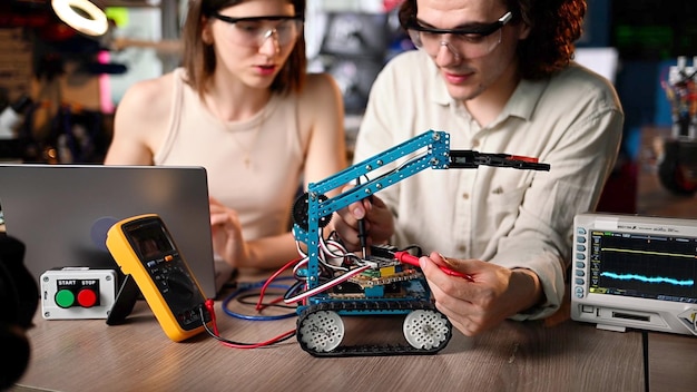 Zwei junge, glückliche Ingenieure reparieren in der Werkstatt ein mechanisches Roboterauto mithilfe der virtuellen VR-Realität