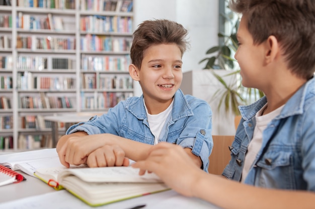 Zwei junge glückliche Jungen, die zusammen in der Bibliothek studieren