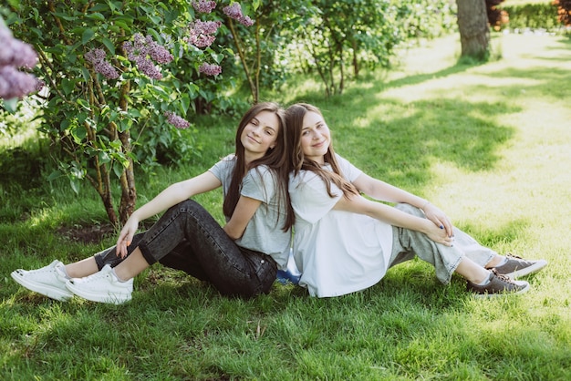 Zwei junge glückliche Mädchen im Teenageralter ruhen im Park auf dem grünen Gras. Weibliche Freundschaft. Weicher selektiver Fokus.