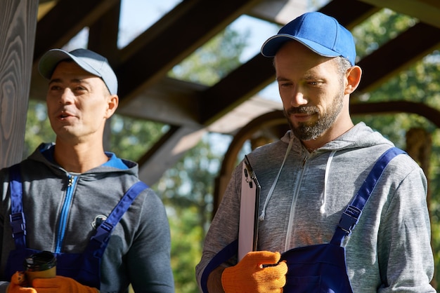 Foto zwei junge handwerker in uniform, die während der arbeit an einem bauprojekt mit papieren im freien stehen