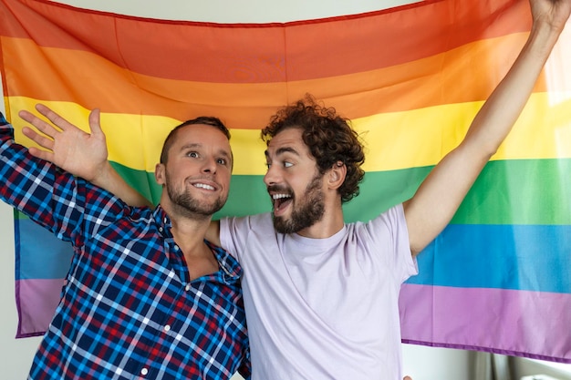 Zwei junge homosexuelle liebhaber, die einander liebevoll betrachten zwei junge männliche liebhaber, die zusammen gegen eine stolzflagge stehen liebevolle junge homosexuelle paare, die einen romantischen moment zusammen teilen