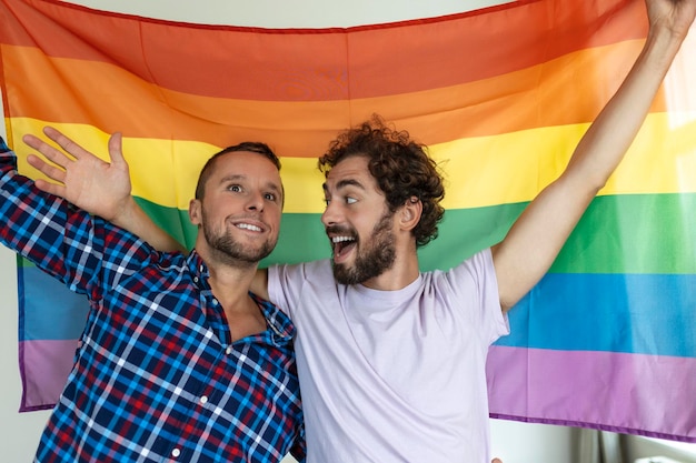 Zwei junge homosexuelle Liebhaber, die einander liebevoll betrachten Zwei junge männliche Liebhaber, die zusammen gegen eine Stolzflagge stehen Liebevolle junge homosexuelle Paare, die einen romantischen Moment zusammen teilen