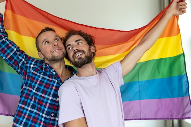 Zwei junge homosexuelle Liebhaber, die einander liebevoll betrachten Zwei junge männliche Liebhaber, die zusammen gegen eine Stolzflagge stehen Liebevolle junge homosexuelle Paare, die einen romantischen Moment zusammen teilen