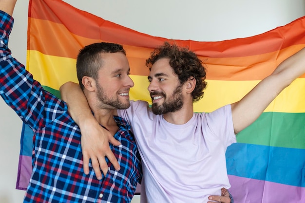 Foto zwei junge homosexuelle liebhaber, die einander liebevoll betrachten zwei junge männliche liebhaber, die zusammen gegen eine stolzflagge stehen liebevolle junge homosexuelle paare, die einen romantischen moment zusammen teilen