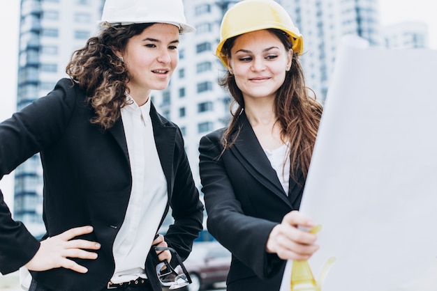 Zwei junge hübsche business-frauen industrie-ingenieure in bau helme auf einem glas gebäude hintergrund. bauplan, architekt, designer, erfolgreich