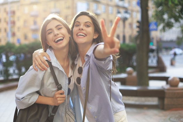 Zwei junge lächelnde Hippie-Frauen in Sommerkleidung, die auf der Straße aufwirft. Weiblich, das positive Gesichtsgefühle zeigt.