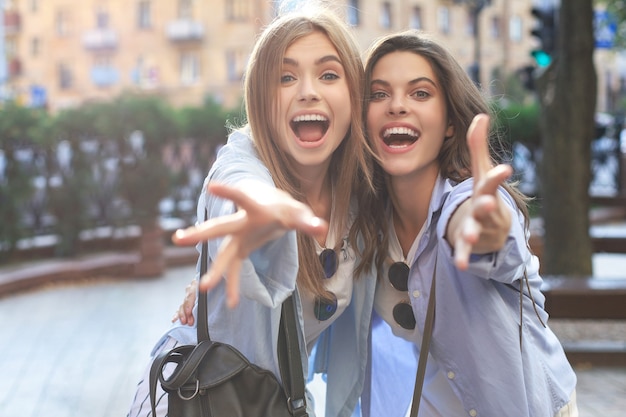 Zwei junge lächelnde Hippie-Frauen in Sommerkleidung, die auf der Straße aufwirft. Weiblich, das positive Gesichtsgefühle zeigt.