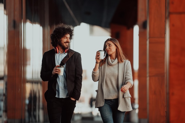 zwei junge leute in einer arbeitspause gehen vor einem modernen unternehmen, in dem sie arbeiten und kaffee trinken.