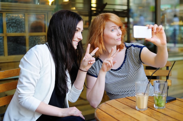 Zwei junge Mädchen, die ein Selbstporträt (selfie) mit intelligentem Telefon nehmen
