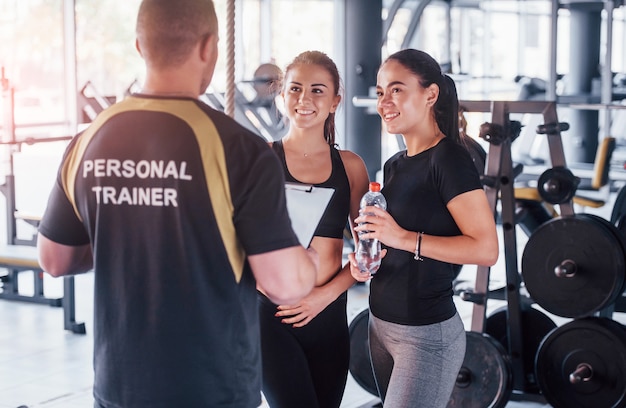 Zwei junge Mädchen in sportlicher Kleidung sind tagsüber zusammen mit ihrem männlichen Personal Trainer im Fitnessstudio.