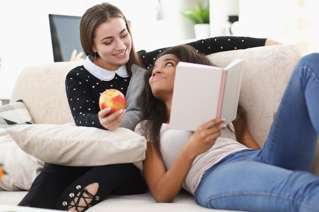 Zwei junge Mädchen sitzen auf der Couch und lesen zu Hause ein Buch