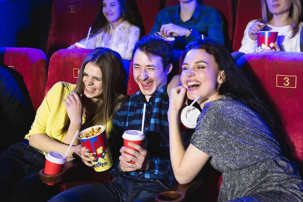 Zwei junge Mädchen und ein Mann, der sich eine Komödie in einem Kino ansieht Junge Freunde, die einen Film im Kino ansehen