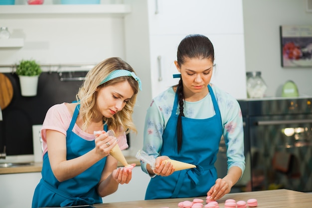 Zwei junge Mädchen verzieren Makronen mit Spritzbeutel gefüllt mit Frischkäse. Backen traditioneller französischer Dessrt