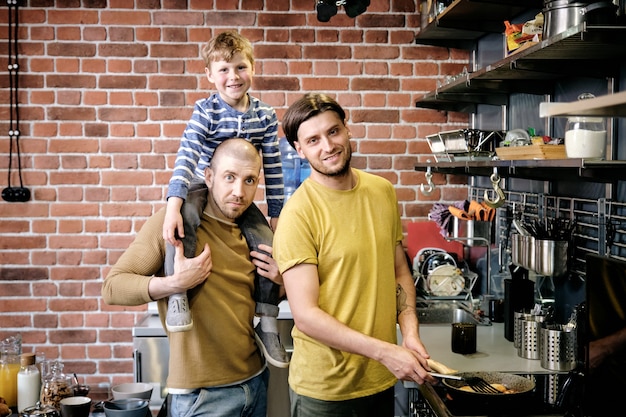 Zwei junge Männer und ihr süßer Sohn kochen in der Küche