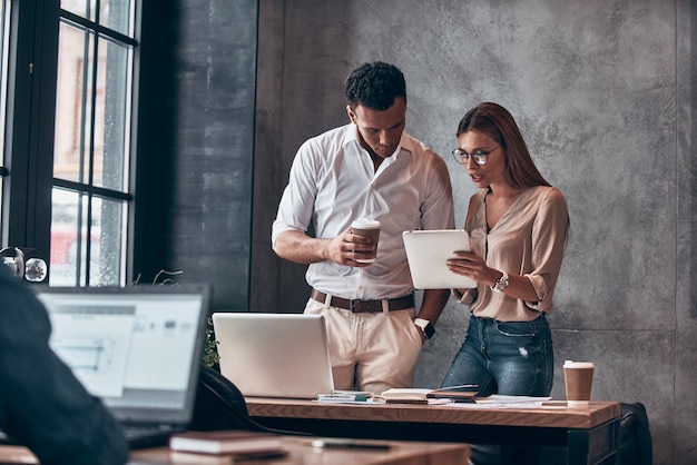 Zwei junge Mitarbeiter in Smart Casual Wear diskutieren über das Geschäft während der Arbeit im Büro