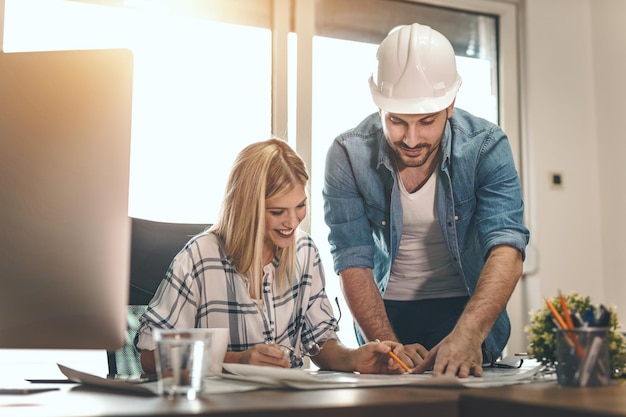 Zwei junge, nachdenkliche Architektenkollegen arbeiten an einem neuen Projekt, analysieren Baupläne und unterhalten sich im Büro darüber.