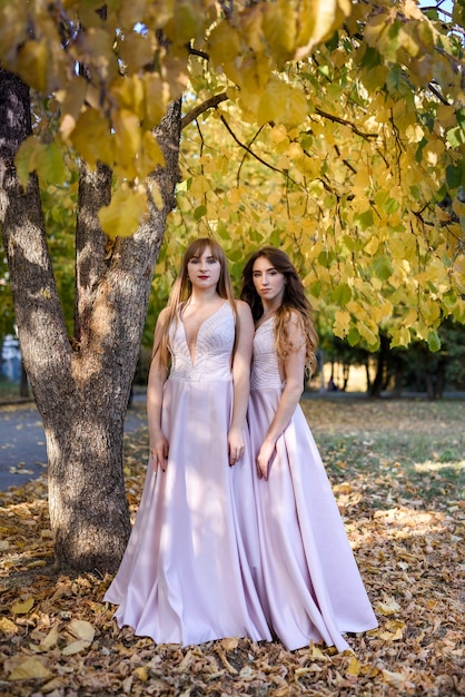 Zwei junge Prinzessinnen, die ein schönes beige Kleid im Herbstpark tragen. Modefoto.