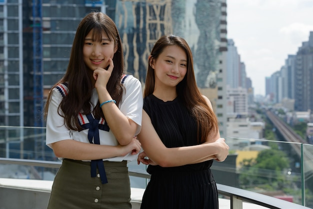 Zwei junge schöne asiatische Teenager-Mädchen zusammen gegen Blick auf die Stadt