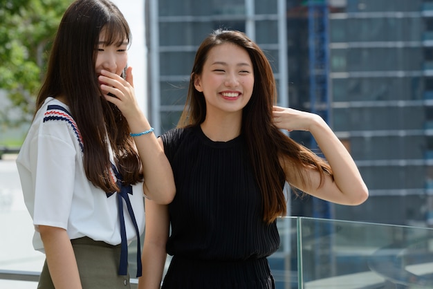 Zwei junge schöne asiatische Teenagerfrauen zusammen gegen Blick auf die Stadt