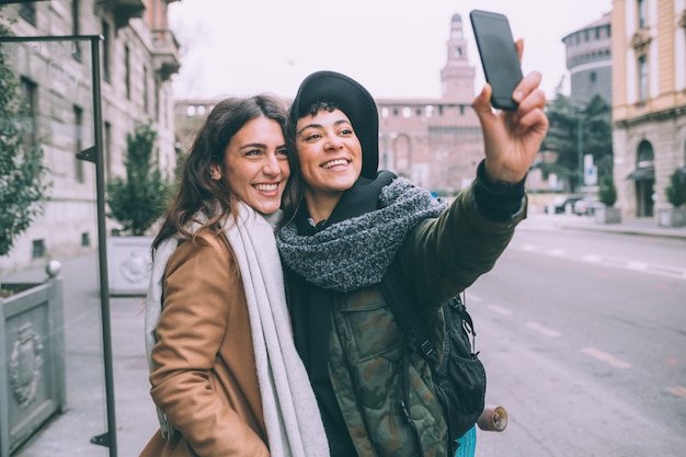 Zwei junge schöne Freundinnen im Freien unter Verwendung des Smartphone, das selfie nimmt