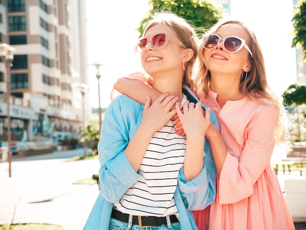 Zwei junge schöne lächelnde Hipster-Frauen in trendiger Sommerkleidung und dressSexy unbeschwerte Frauen posieren auf dem Straßenhintergrund Positive reine Models, die sich bei Sonnenuntergang amüsieren, umarmen und verrückt werden