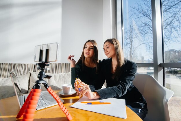 Zwei junge schöne Mädchen sitzen in einem Café, nehmen Videoblogs auf und kommunizieren in sozialen Netzwerken.