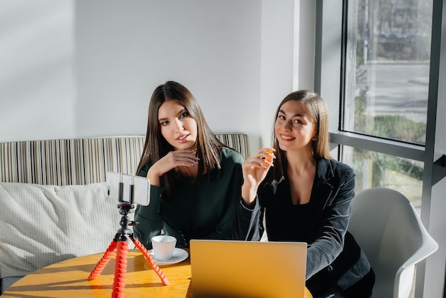 Zwei junge schöne Mädchen sitzen in einem Café, nehmen Videoblogs auf und kommunizieren in sozialen Netzwerken.