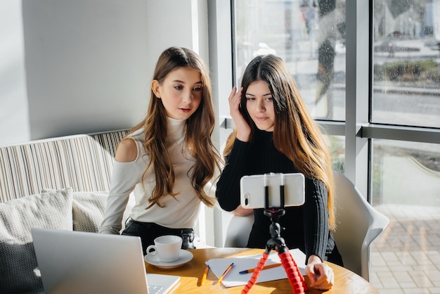 Zwei junge schöne Mädchen sitzen in einem Café, nehmen Videoblogs auf und kommunizieren in sozialen Netzwerken.