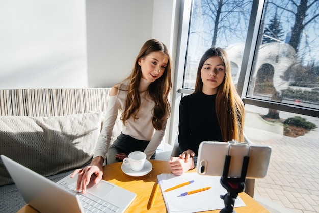 Zwei junge schöne Mädchen sitzen in einem Café, nehmen Videoblogs auf und kommunizieren in sozialen Netzwerken.