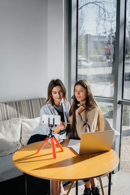 Zwei junge schöne Mädchen sitzen in einem Café, nehmen Videoblogs auf und kommunizieren in sozialen Netzwerken.