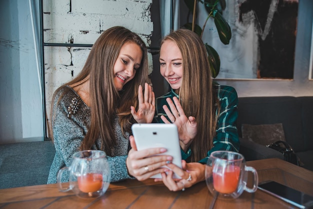 Zwei junge Schönheitsfrauen sprechen per Video-Chat mit Tablet. im Café sitzen und Früchtetee trinken