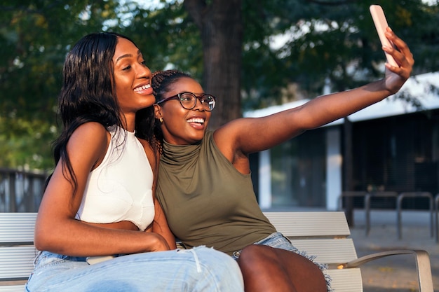 Zwei junge schwarze Frauen lächeln glücklich, während sie ein Selfie-Foto mit dem Handy machen
