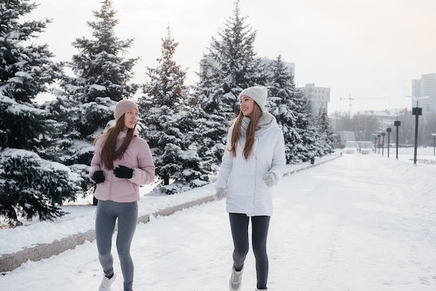 Zwei junge sportliche Mädchen, die an einem sonnigen Wintertag im Park laufen. Eine gesunde Lebensweise.