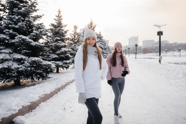 Zwei junge sportliche Mädchen, die an einem sonnigen Wintertag spazieren gehen und Sport treiben. Eine gesunde Lebensweise.