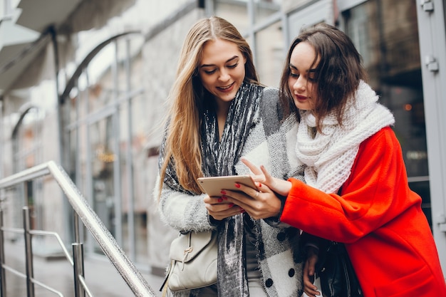 Zwei junge stilvolle Geschäftsfrauen, die in einer Herbststadt stehen und die Tablette verwenden