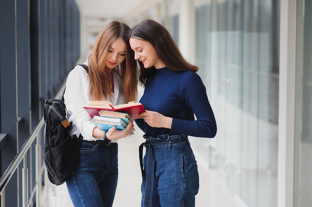 Zwei junge Studentinnen, die mit Büchern und Taschen im Flur stehen