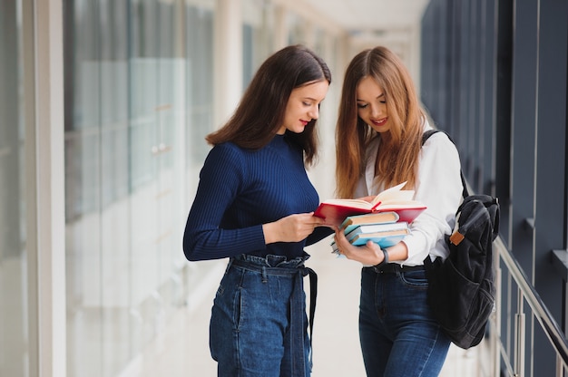 Zwei junge Studentinnen, die mit Büchern und Taschen im Flur stehen