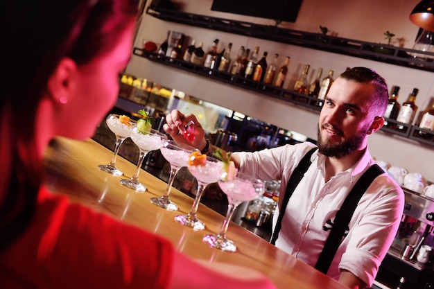 Zwei junge süße Mädchen trinken Cocktails in einem Nachtclub oder einer Bar, haben Spaß, lächeln und sprechen mit dem Barkeeper