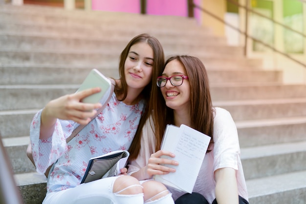 Zwei junge süße Schulmädchen, die vorne auf der Schule stehen und über Hausaufgaben sprechen.