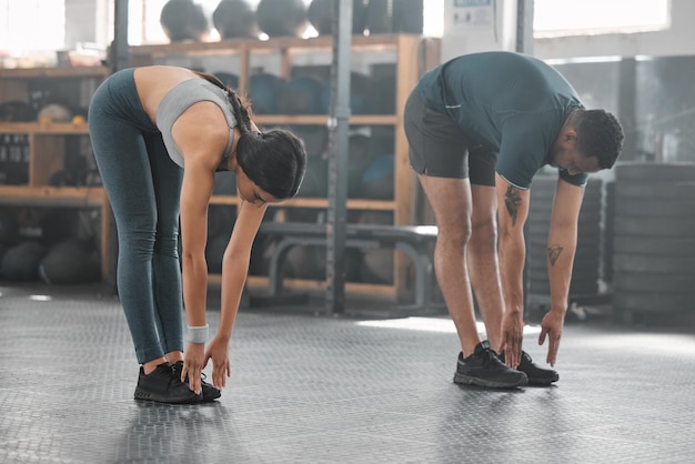 Zwei junge und fitte Freunde, die sich beim Aufwärmen dehnen und trainieren, während sie zusammen in einem Fitnessstudio trainieren