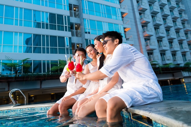 Zwei junge und hübsche asiatische chinesische Paare oder Freunde trinken Cocktails in einer luxuriösen und schicken Hotel-Poolbar