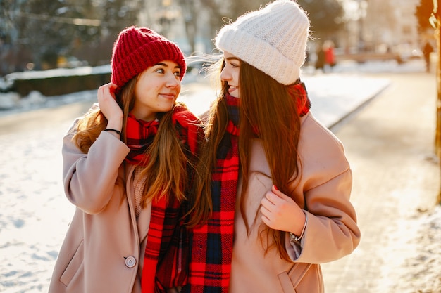 Zwei junge und hübsche Mädchen in den Winterhüten, die in eine Winterstadt gehen
