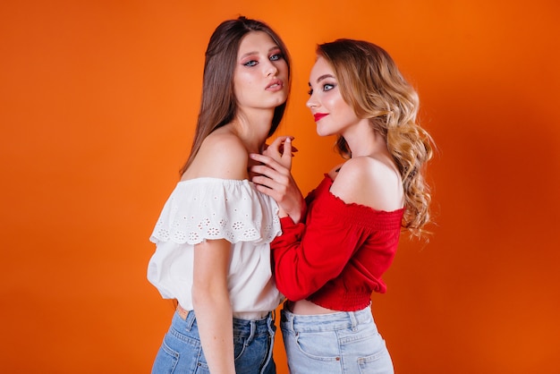 Zwei junge und schöne Mädchen in einem Studio auf einem orange Hintergrund.