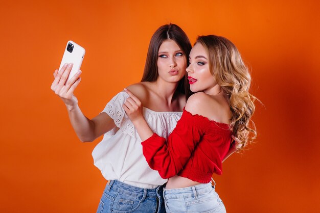 Zwei junge und schöne Mädchen machen ein Selfie und schauen sich das Telefon im Studio auf lila Hintergrund an. Mädchen für Werbung.