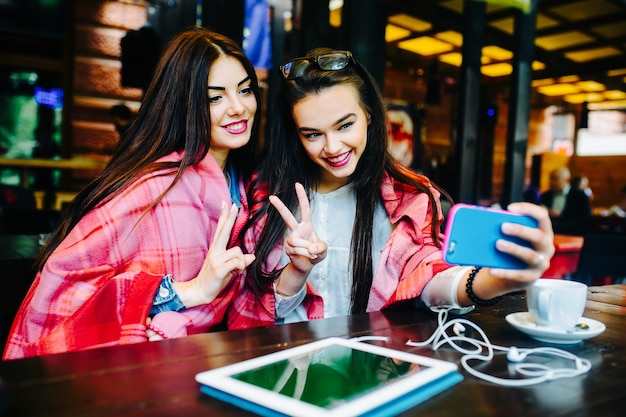 Zwei junge und schöne Mädchen sitzen am Tisch und machen Selfie im Café