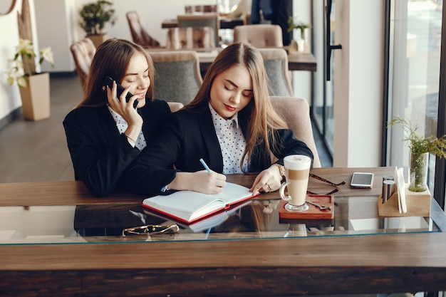 zwei junge und stilvolle Geschäftsfrauen, die am Schreibtisch und am Arbeiten des Cafés sitzen