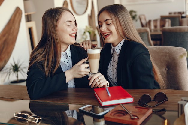 zwei junge und stilvolle Geschäftsfrauen, die am Schreibtisch und am Arbeiten des Cafés sitzen