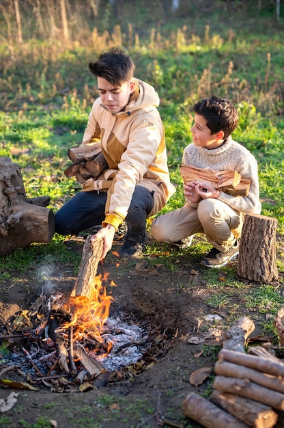 Zwei Jungen auf einem Picknick entzünden ein Lagerfeuer mit Stämmen, grünem Gras