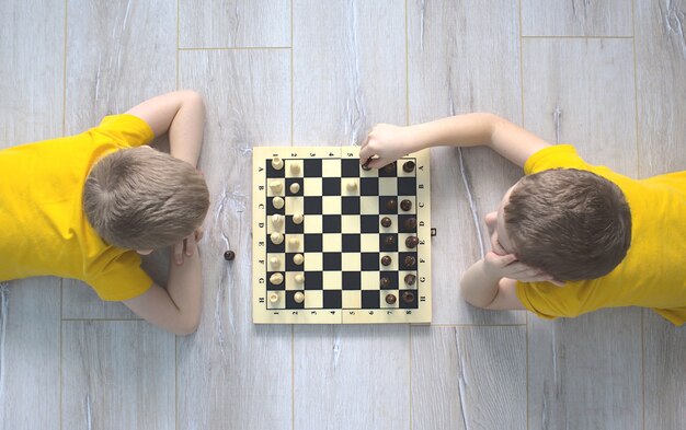 Foto zwei jungen in gelben t-shirts spielen schach auf dem boden