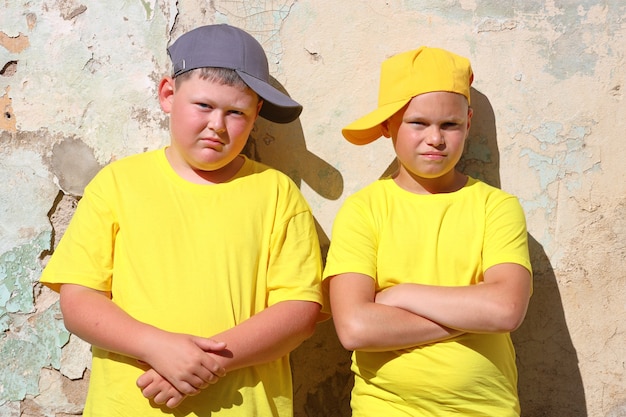 Zwei Jungen in gelben T-Shirts stehen in der strahlenden Sonne an einer Wand. Foto in hoher Qualität